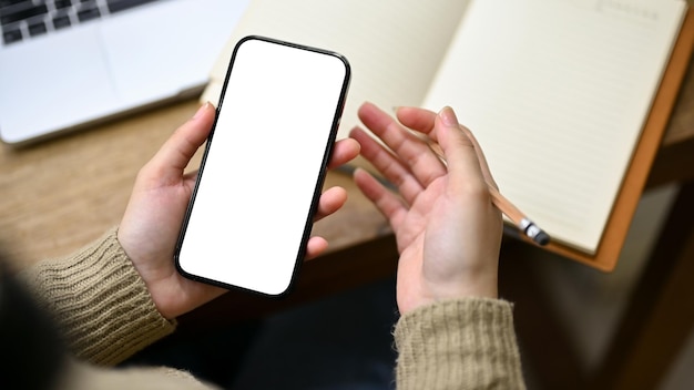 Closeup shot of a woman scrolling on her phone at her desk phone white screen mockup