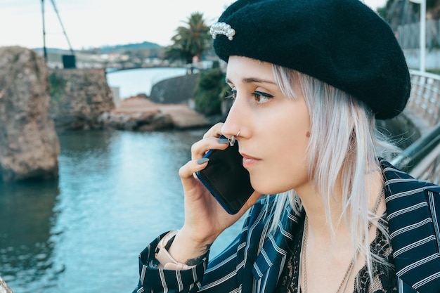 Closeup shot of a young blonde female with a hat talking on the phone by the river