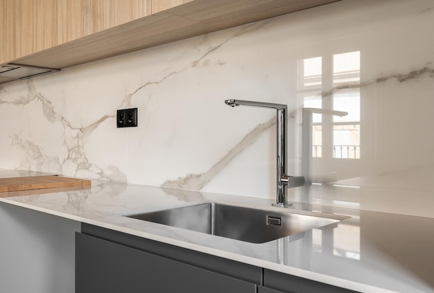 Closeup side view of contemporary design square metal sink embedded in beautiful light gray marble