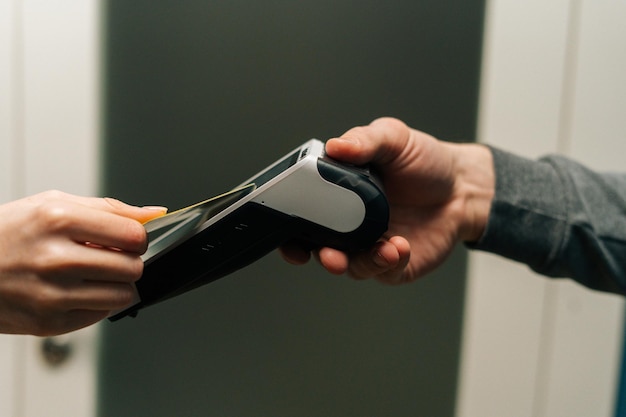 Closeup side view of unrecognizable courier male giving POS wireless terminal to making contactless payment via credit card to young female customer