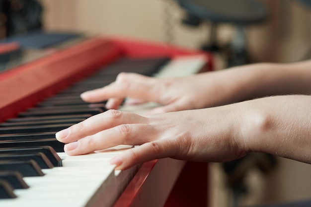 Closeup side view of a womans hand playing a red electronic piano