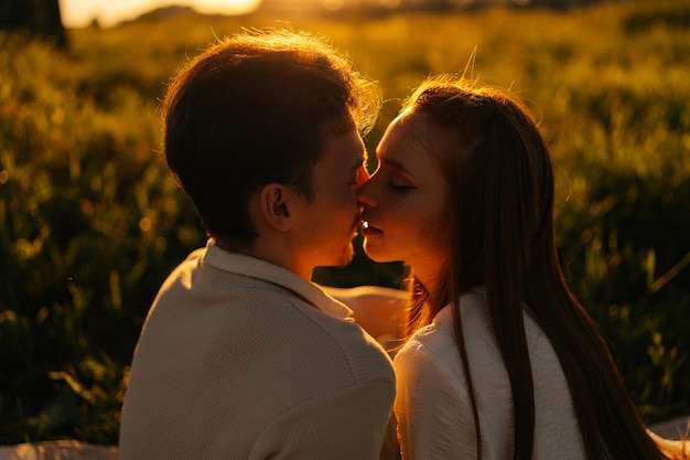 Closeup silhouette view of loving young couple sitting hugging and kissing on beautiful meadow with green grass having picnic date