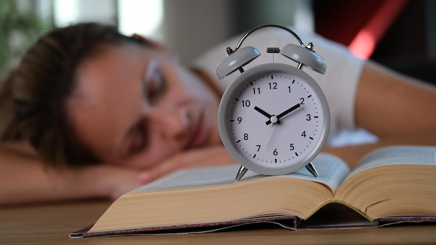 Closeup of sleeping female at table near grey alarmclock on big book time to education learning