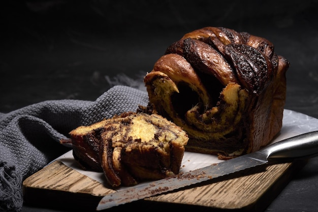 Closeup of a sliced chocolate babka and bread knife on a wooden board