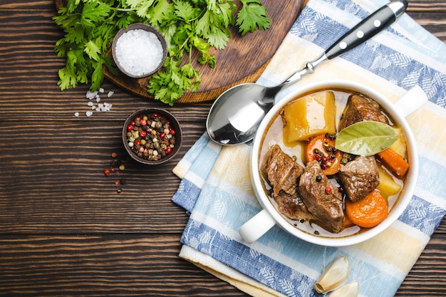 Closeup of slow cooked meat stew ragout in bowl with beef, potato, broth on wooden rustic background