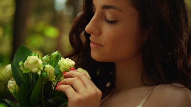 Closeup smiling bride admiring flowers in garden Beautiful woman holding white roses in park Portrait of relaxed lady standing with bouquet outdoors