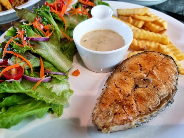 Closeup Snapper fish steak with tarragon sauce salad and french fries on the white plate