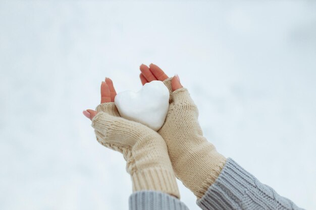 Closeup Snow heart in hands in knitted gloves on the background of snow cover Valentine39s Day