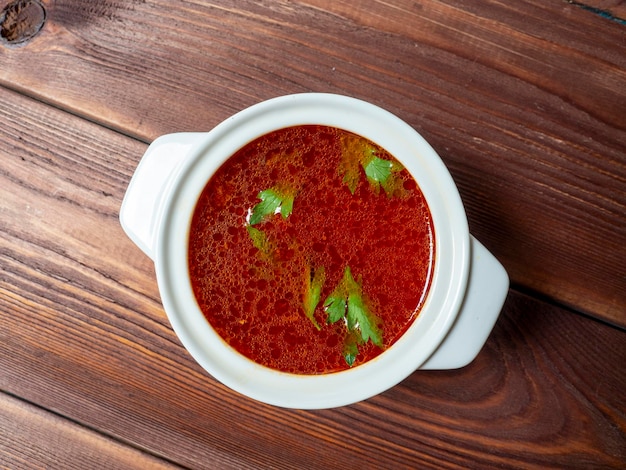 Closeup of soup borscht in a white ceramic soup bowl on a wooden background Traditional soup for Russia and Ukraine Greens float on top of the soup Top view flat lay