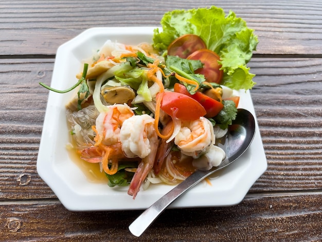 Closeup of the spicy Thai seafood salad served in the white plate for an appetizer in the Thai restaurant, above view with the copy space.