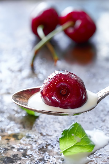 Closeup on a spoon with cream and dark cherry with more cherries and fresh mint leaves