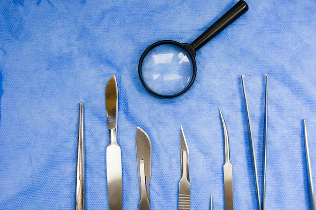 Closeup of a stainless dissection kit near a magnifier on a blue surface