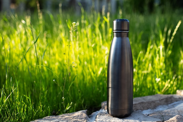 Closeup of steel thermo water bottle of black on background of green grass with copy space. Reusable bottles zero waste eco concept plastic free.