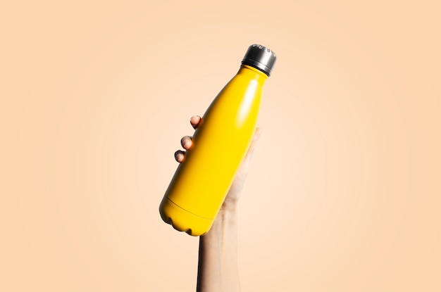 Closeup of steel thermo water bottle in female hand isolated on pastel yellow background