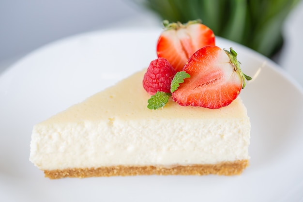 Closeup of strawberry cheesecake on a white plate on a cake stand