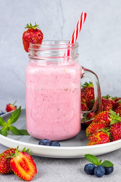 Closeup of a strawberry smoothie or milkshake with berries in a glass jar on a gray concrete background Vegetarian healthy drink