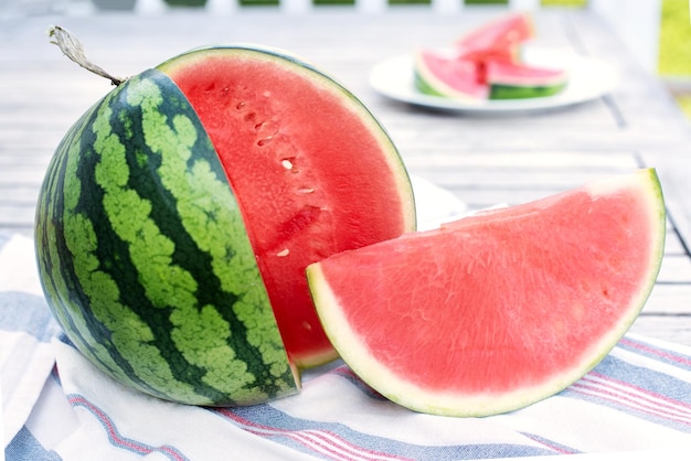 Closeup of striped watermelon and slice on wooden table outdoors