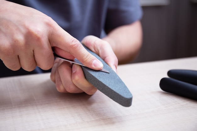 Photo closeup strong male hands sharpen a kitchen metal knife with a grindstone home household knife sharpening