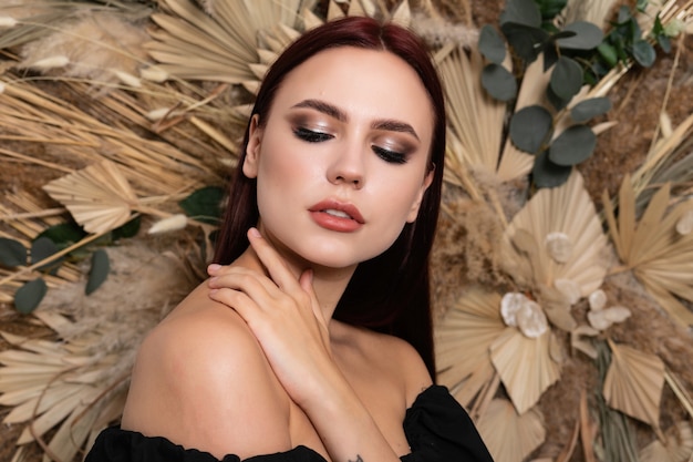 Closeup studio portrait of beautiful brunette woman girl with burgundy lips on a background of spring dry field flowers. open shoulders