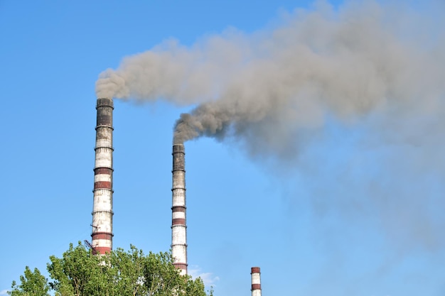 Closeup of thermal power plant high pipes with black smoke moving upwards polluting atmosphere Production of electrical energy with fossil fuel concept