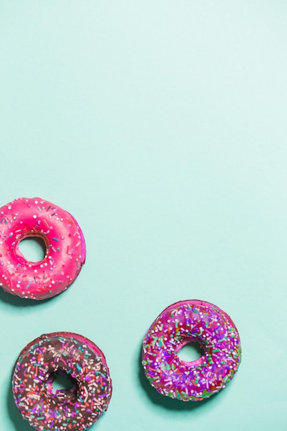 Closeup of three multicolored glazed sweet donuts on a blue background, top view, copy space. Food, restaurant, bakery concept