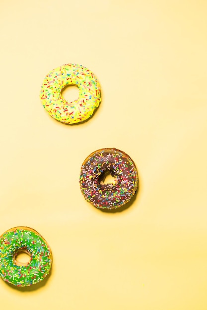 Closeup of three multicolored glazed sweet donuts on a yellow background, top view