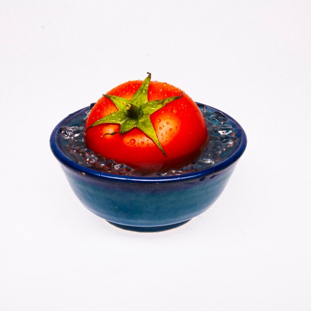 Closeup of a tomato in a small bowl filled with water isolated on the white background