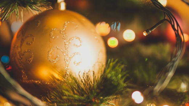 Closeup toned image of golden Christmas ball and glowing light garlands on Xmas tree