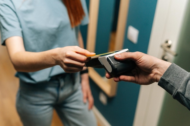 Closeup top view of unrecognizable courier male giving POS wireless terminal to making contactless payment via credit card to young female customer