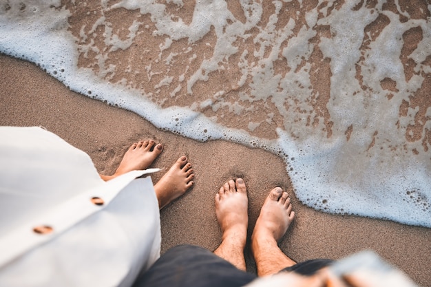 Closeup traveler man and woman foot of relaxing on beach with sea wave in summer, Holiday travel vacation concept