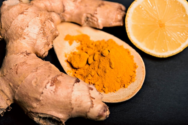 Closeup turmeric curcumin powder in wooden spoon with fresh rhizome on wood background