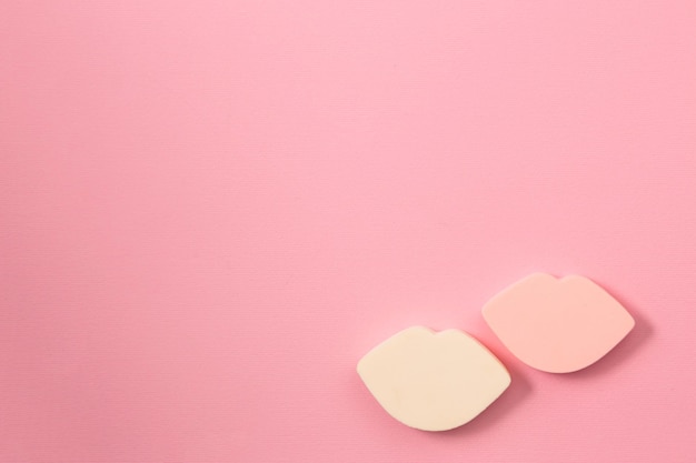 Closeup of two beautiful lip shaped makeup sponges on bright pink background with copy space, top view. Cosmetics, makeup, beauty, fashion, youth, care concept