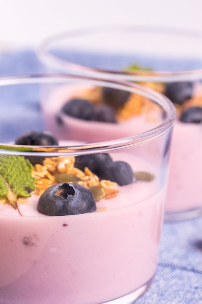 Closeup of two glasses of strawberry yogurt with blueberries and cereal on a blue tablecloth