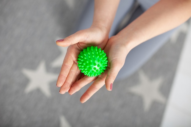 Closeup two womens hands hold a green spiked massage ball