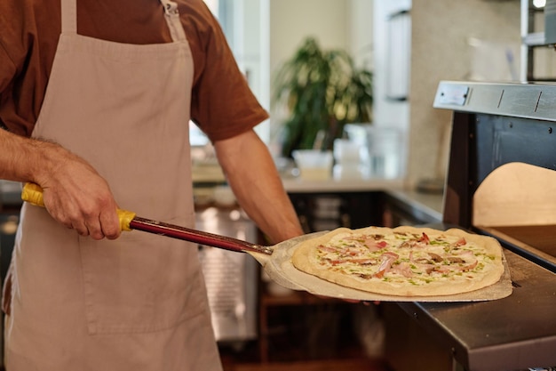 Closeup of unknown caucasian cook taking pizza from oven using pizza peel