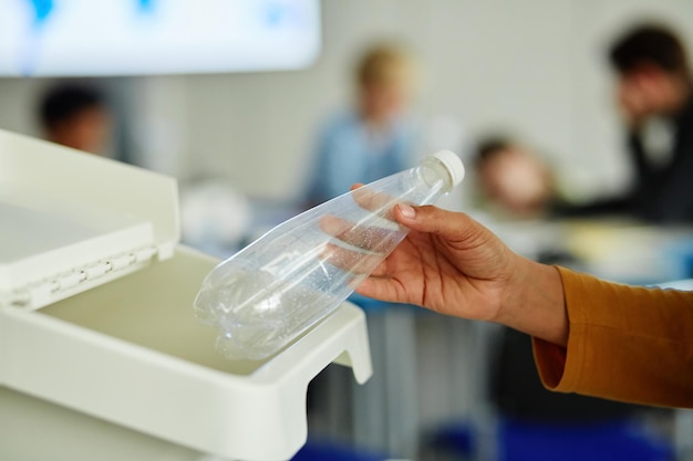 Closeup of unrecognizable child using using waste sorting bins in school and putting plastic bottle