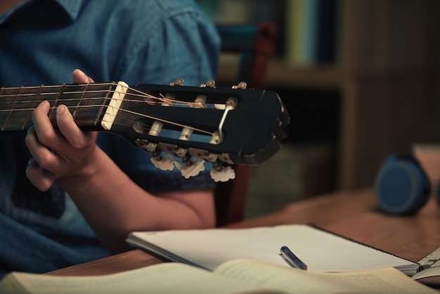 Closeup of unrecognizable man sitting at table and learning to play guitar using manual at night