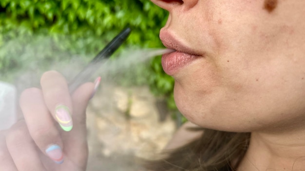 Closeup of an unrecognizable woman smoking and expelling smoke from an electronic cigarette and on the street