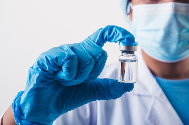 Closeup vial of covid-19 vaccine in hand of professional scientist or doctor in laboratory for treatment with mask gloves and lab coat on white background. Health business and industry concept.