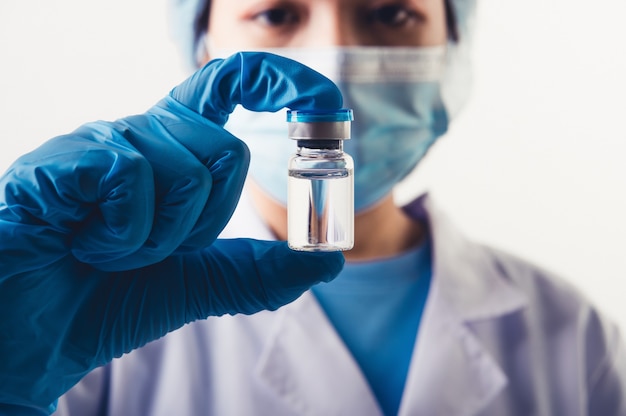 Closeup vial of covid-19 vaccine in hand of professional scientist or doctor in laboratory for treatment with mask gloves and lab coat on white background. Health business and industry concept.