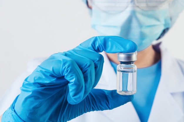 Closeup vial of covid-19 vaccine in hand of professional scientist or doctor in laboratory for treatment with mask gloves and lab coat on white background. Health business and industry concept.