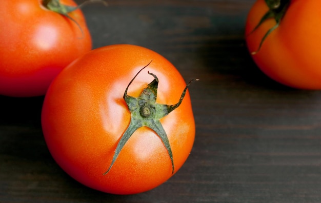 Closeup of vibrant red tomatoes scattered on dark brown wooden background