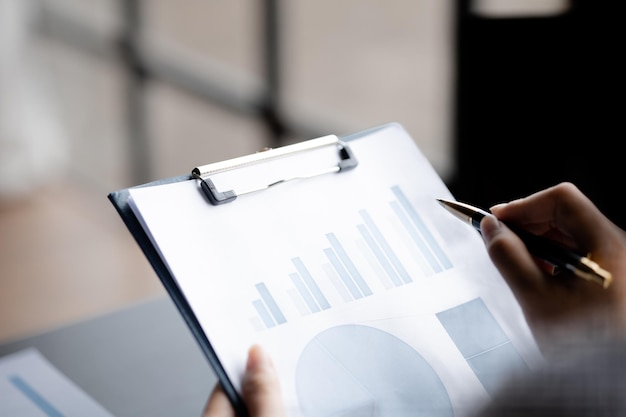 A closeup view of a businessman pointing at a bar chart on a company financial document prepared by the Finance Department for a meeting with business partners Financial concept