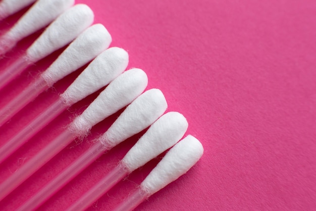 Closeup view from above on cotton buds laid in a diagonal line on pink background