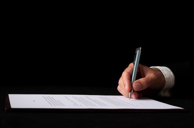 Closeup view of a hand of a businessman signing a document or contract. Over black background.