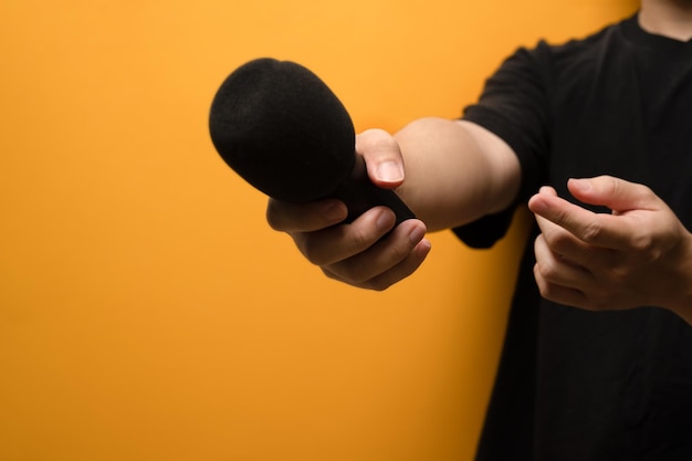 Closeup view of hand holding microphone and towards the camera over yellow background with copy space