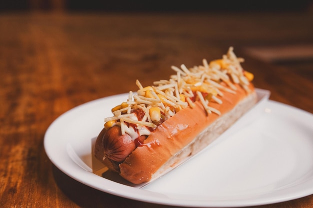 Photo closeup view of a hot dog topped with french fries on a plate on top of a wooden table