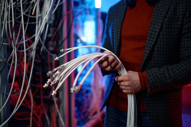 Closeup view of IT man with bunch of cables in hands while working at network server room. Engineer setting farm of mining cryptocurrency