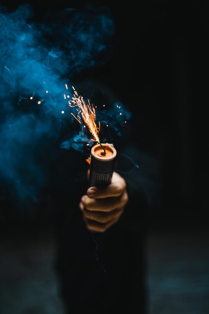 Closeup view of a man holding an explosive firework with smoke coming out of it in his hands