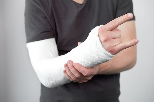 Closeup view of man's hand with plaster cast on a white wall background.